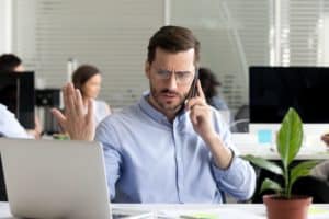 Angry business man talking on phone disputing looking at laptop.