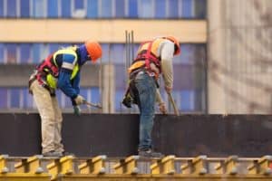 Two Alabama workers with hammers build scaffolding at a construction site.