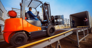 Forklift is putting cargo from warehouse to truck outdoors.