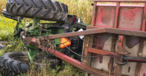 A farm tractor and the attached cart lay on their side.